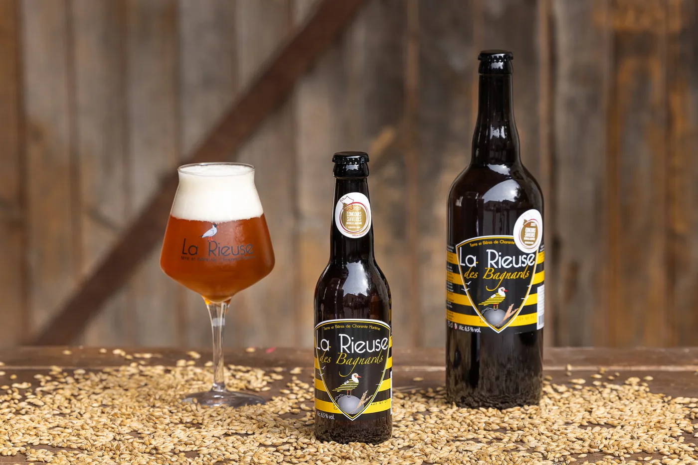 Bières de ferme bio La Rieuse et un verre de bière posés sur des grains d'orge